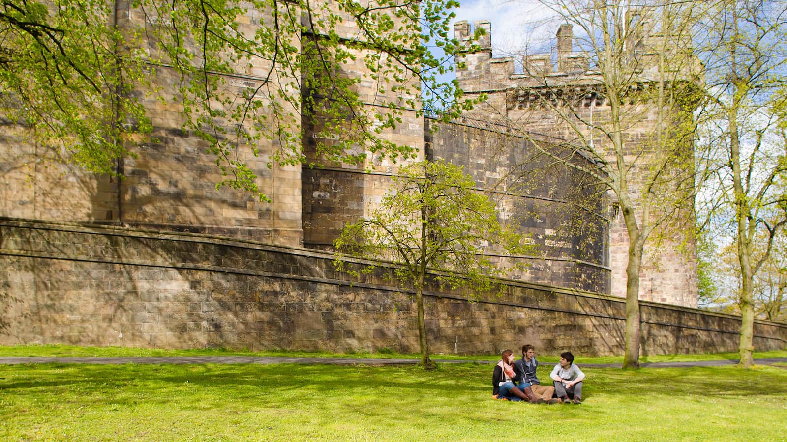 Students sit on the grass outside the walls of СʪƵ Castle